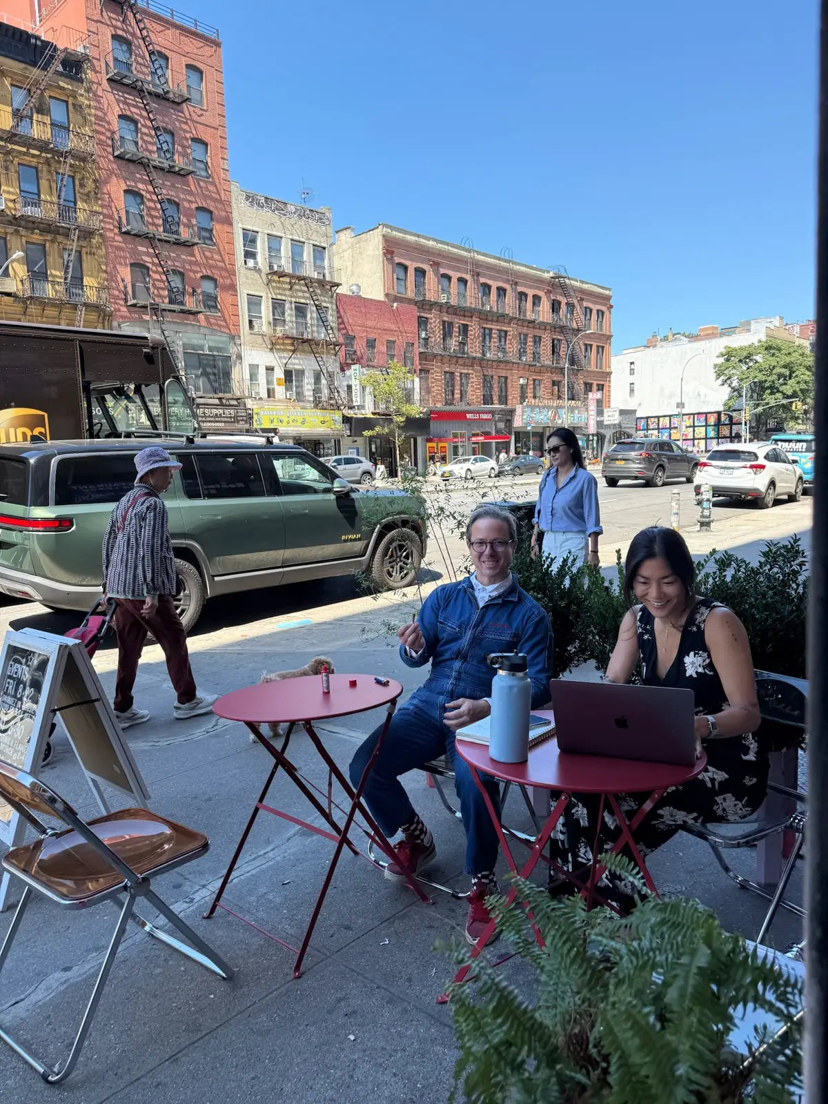 Sidewalk seating with red bistro tables outside Mighty Lucky at 259 Bowery on a sunny day